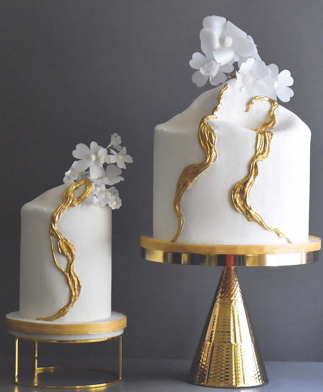 Elegant wedding cakes are designed with simple white flowers and gold accents. 