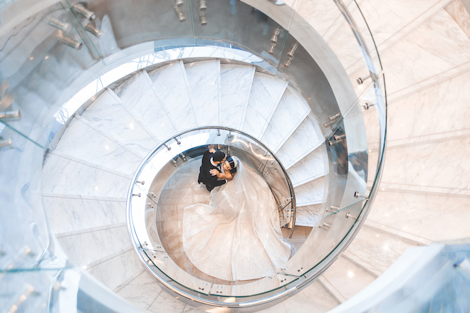 A couple in the center of a white marble staircase at the Post Oak Hotel at Uptown Houston. 