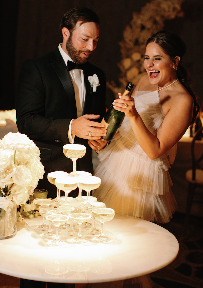 The bride and groom celebrate with pouring champagne over a champagne tower. 