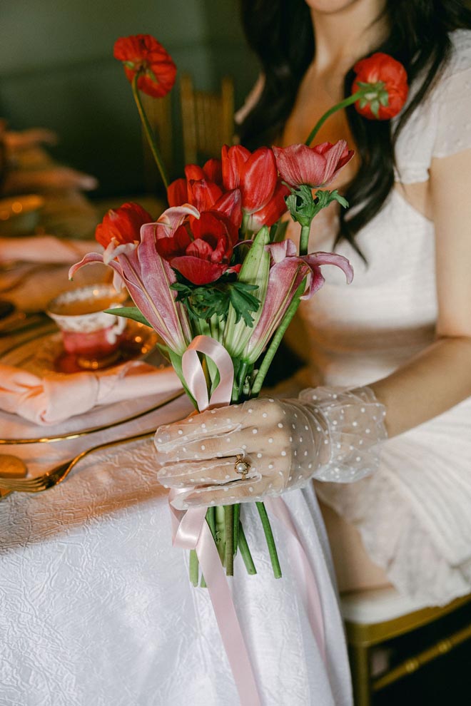 The bride holds a red floral bouquet at her vintage bridal shower.