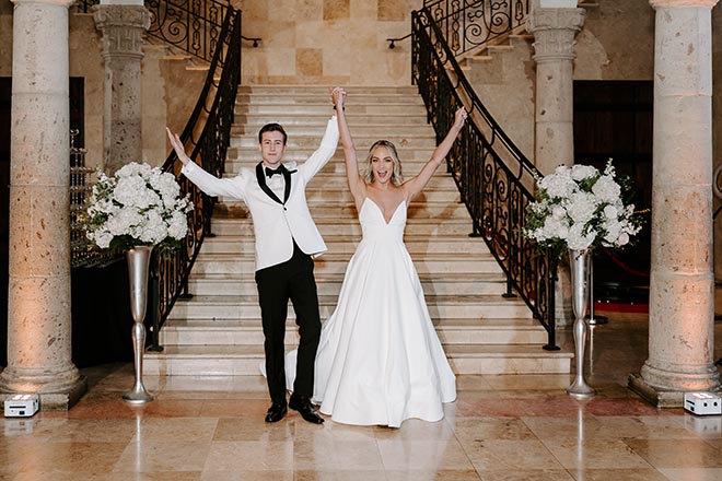 The bride and groom raising their hands as they walk down the grand staircase of The Bell Tower on 34th. 