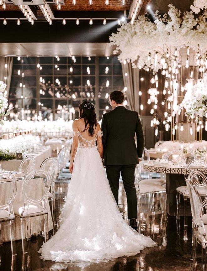 The bride and groom walk around their Broadway-Styled reception while holding hands. 