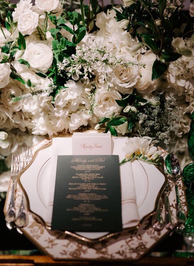 Green and gold wedding stationery are placed on top of the table settings.