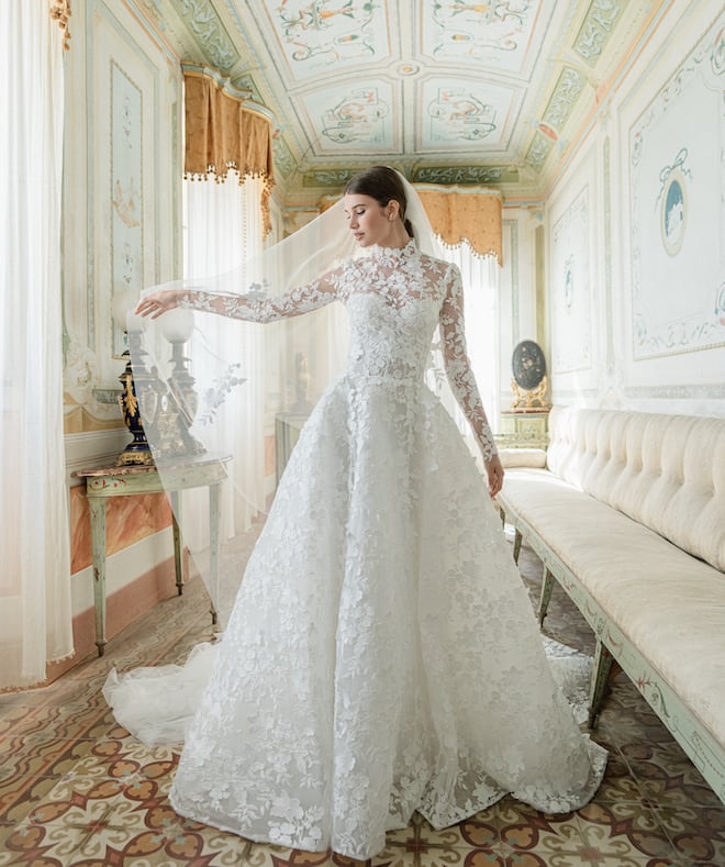 Model wearing an all lace long sleeve gown with a high neck and a traditional tulle veil. 