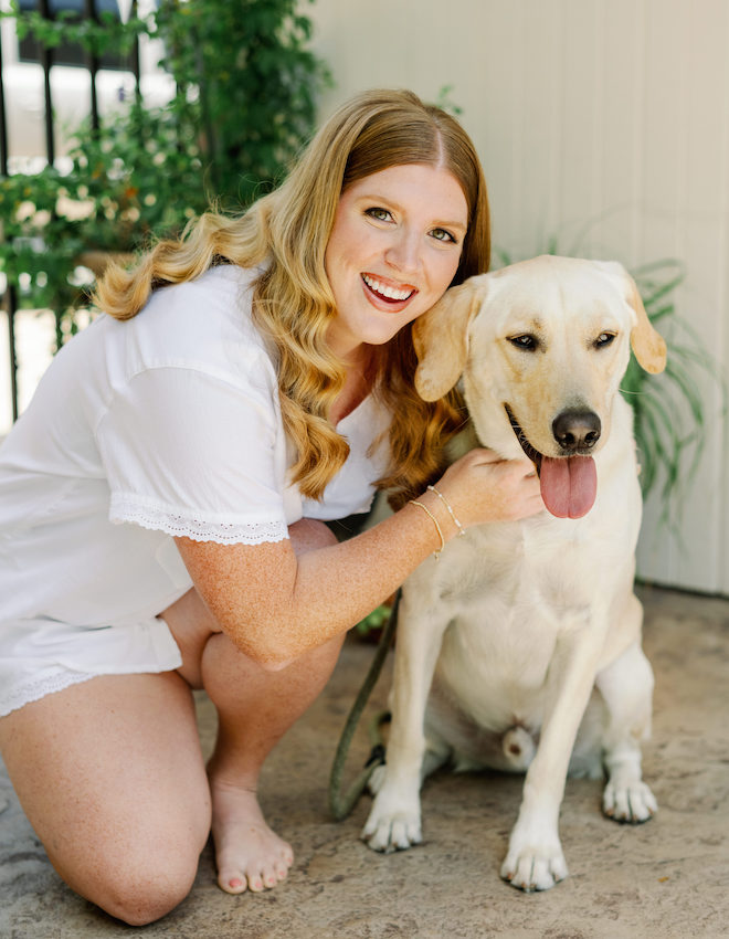 A bride in white pajamas posing with her yellow lab before the wedding. 