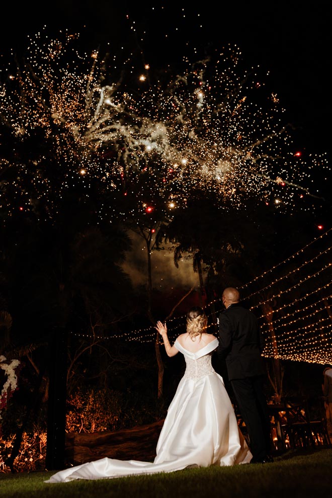 The bride and groom look up at the sky to watch fireworks.