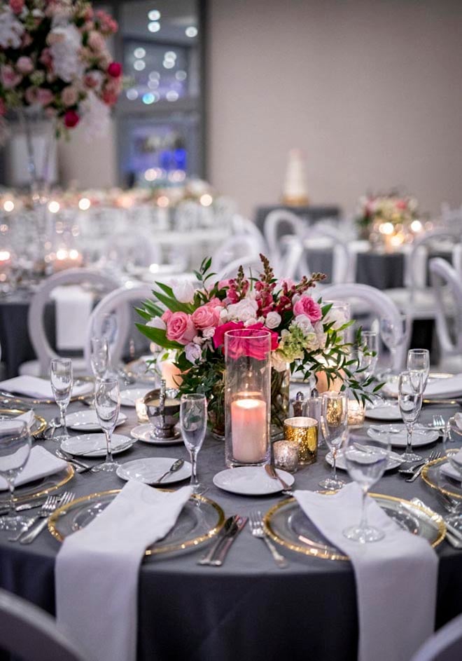 Pink floral centerpieces, gold chargers and navy linens decorate the wedding reception tables.