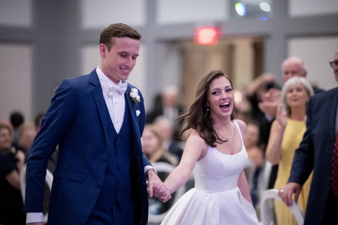 The bride and groom hold hands as they walk onto the dance floor at their ballroom wedding reception. 