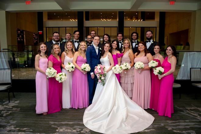 The wedding party smile next to the bride and groom wearing pink and navy attire. 