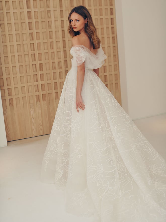 Flowy gown decorated with a delicate flower contour throughout, has a sweetheart corset and an off- the shoulder element.