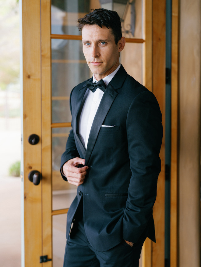 The groom wearing a black tuxedo with a black bowtie. 