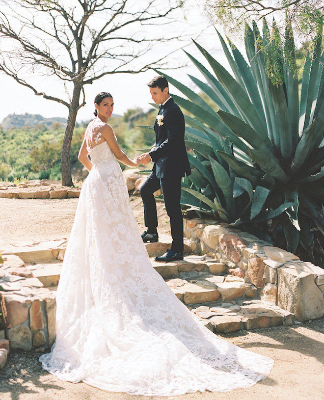 A bride and groom holding hands while walking up stone steps in the desert of Ojai California. 
