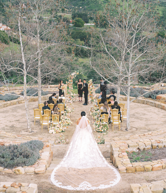 A bride walking down a floral adorned aisle to a floral broken arch altar where the groom is waiting. 