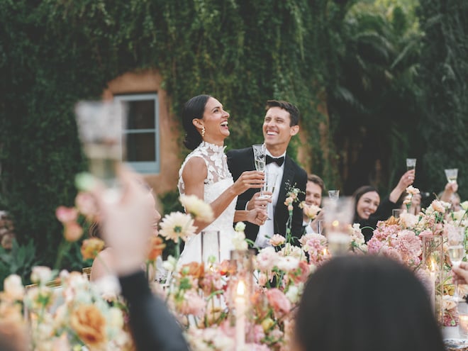 The bride and groom laughing with guests as they raise their glasses in the air. 