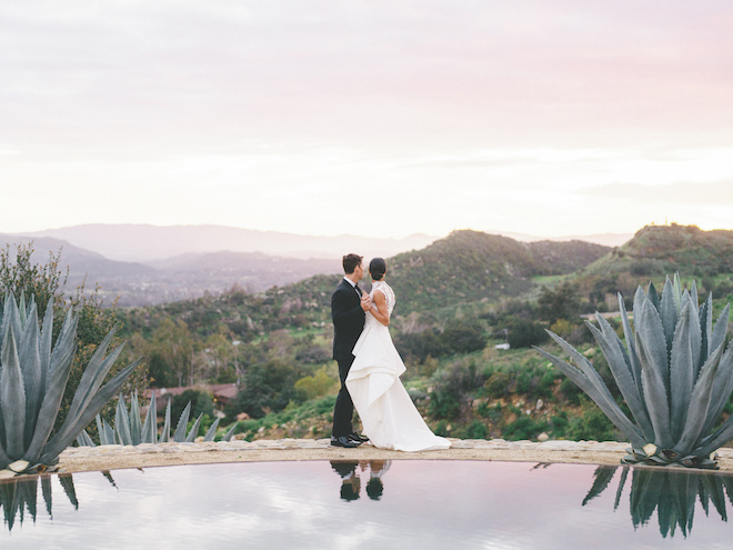 The bride and groom standing close and holding hands looking out at the mountains of Ojai. 
