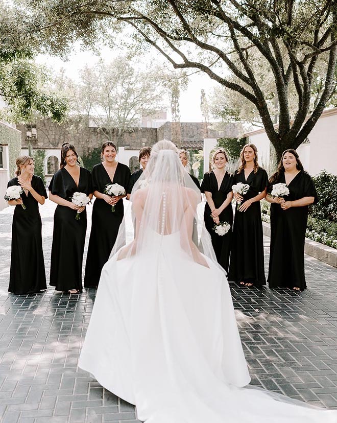 The bride standing in front of her bridesmaids in black dresses showing her wedding gown for the first time. 