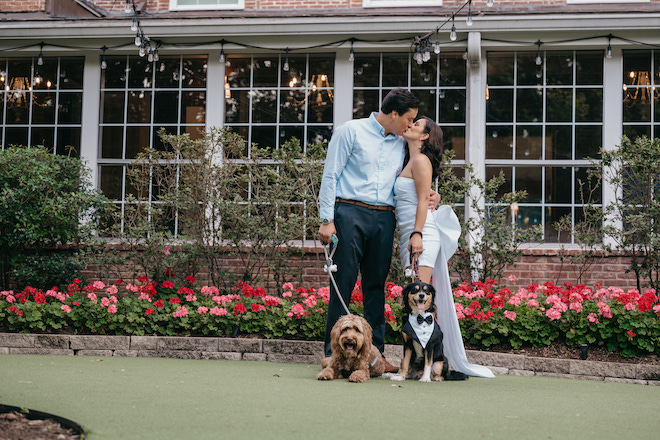 Couple kissing in front of the Houstonian Hotel, Club & Spa while holding the leashes of two dogs in tuxes. 