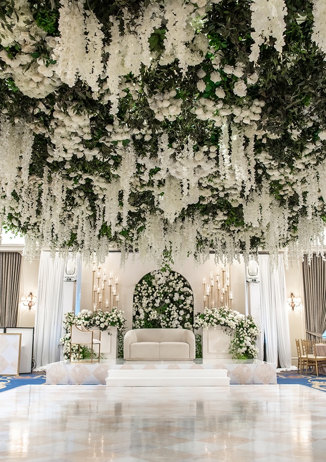 White florals and greenery installations hang from the ceiling at the ballroom reception.