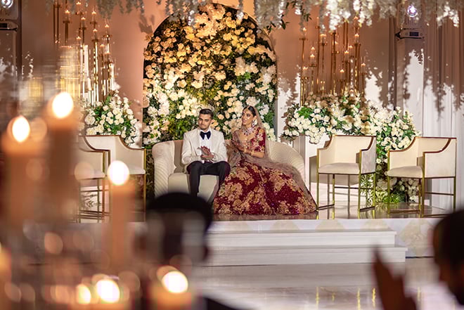The bride and groom sit on a stage at their South Asian wedding reception.