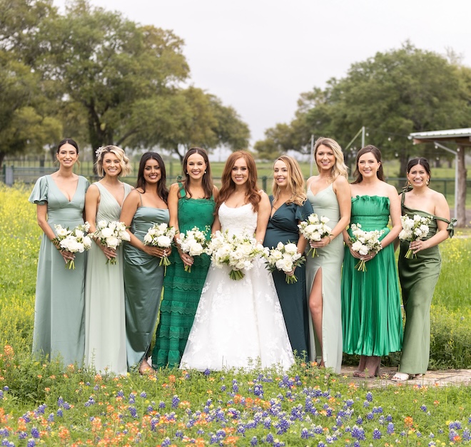 The bride standing with her bridesmaids in mismatched green dresses.