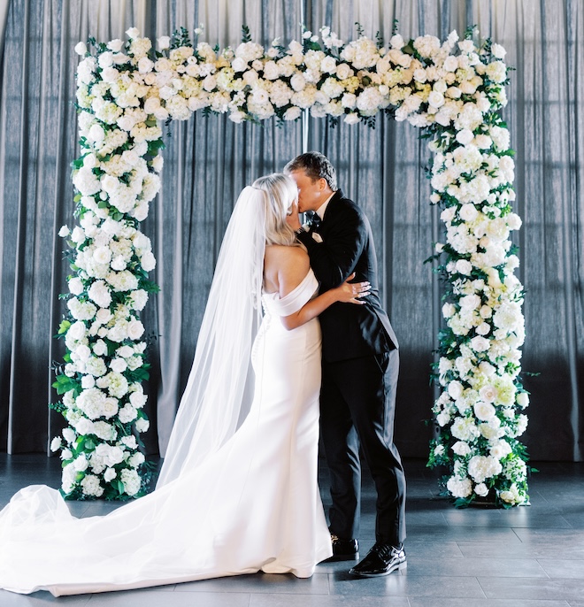 The bride and groom kissing at the white floral covered altar.