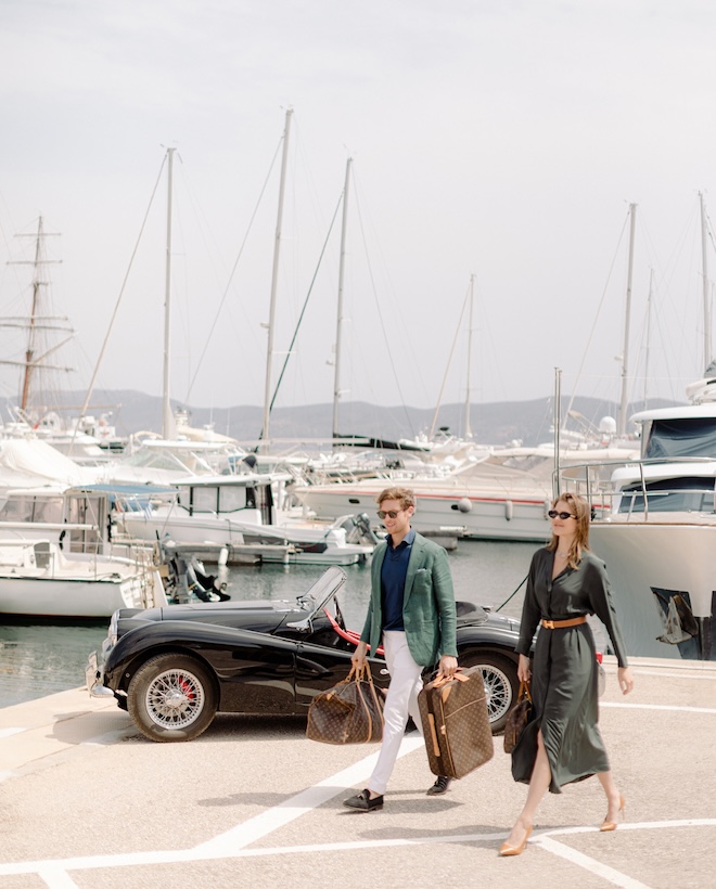 The couple walk with their luggage in a marina.