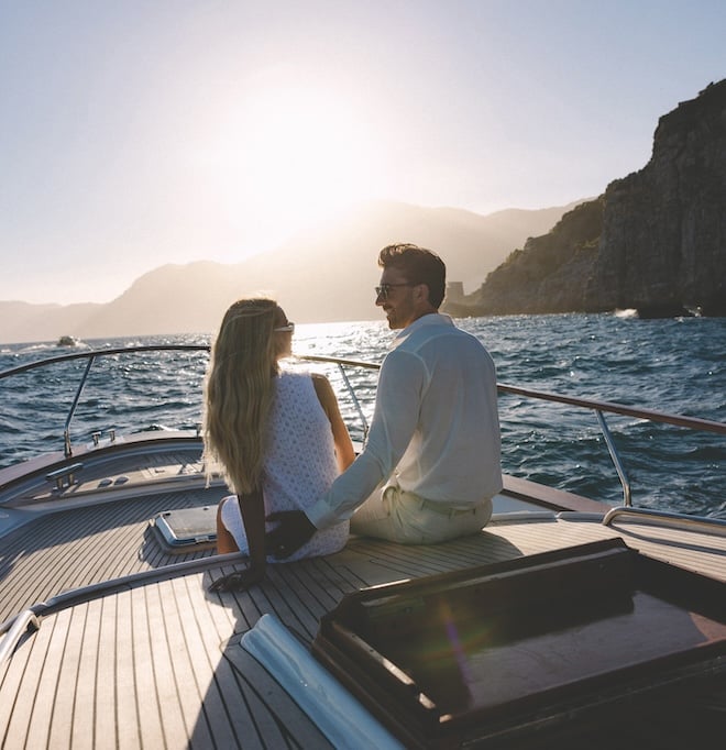 A couple smiling at each other while on a boat in the middle of the sea. 