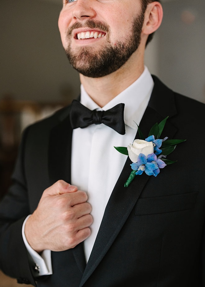 The groom wears a white and blue floral boutonniere on his tuxedo.