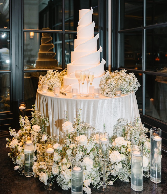 A six-tier white cake surrounded by white florals and baby's breath.