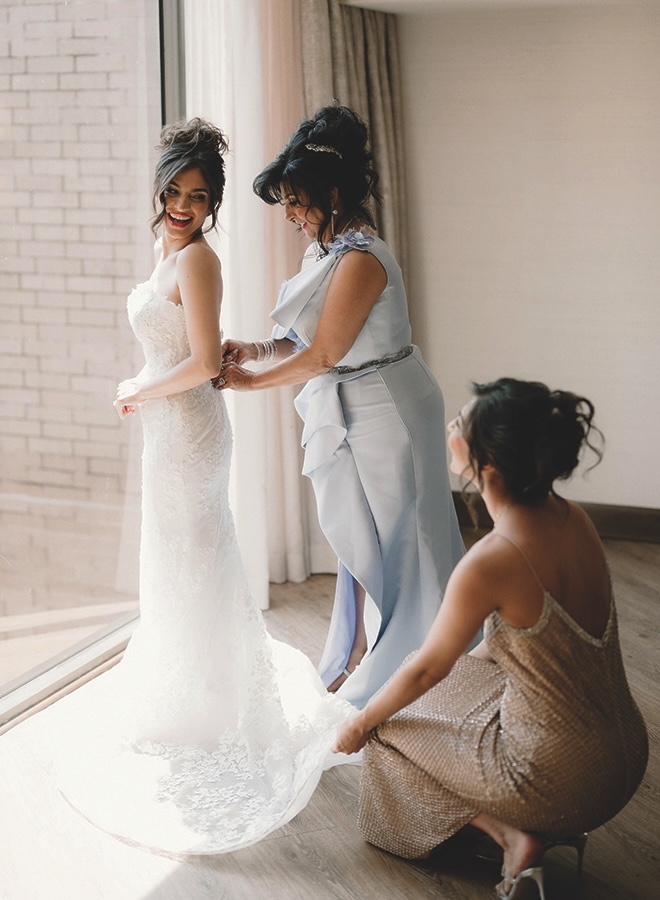 The mother of the bride and a bridesmaids helps the bride with her wedding dress.
