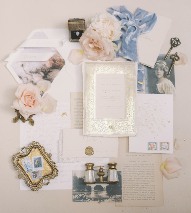 A gold, cream and white invitation suite with vintage accessories around it.