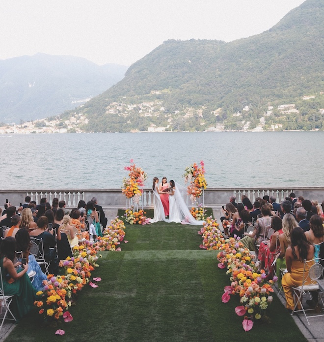 The guests sitting while the brides exchange vows with Lake Como in the background.