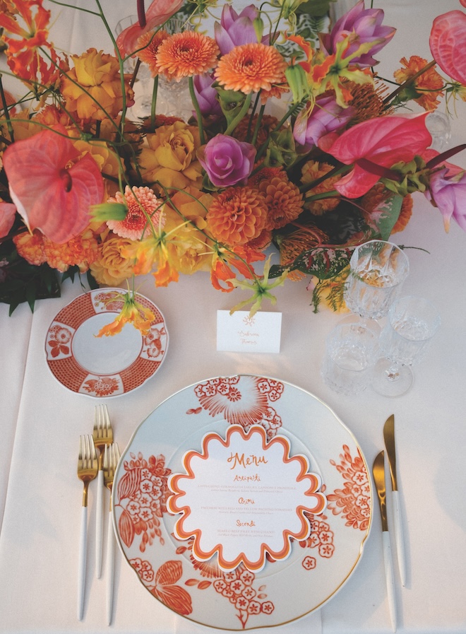 Bold florals with orange and white patterned plates with a orange and white menu on it.