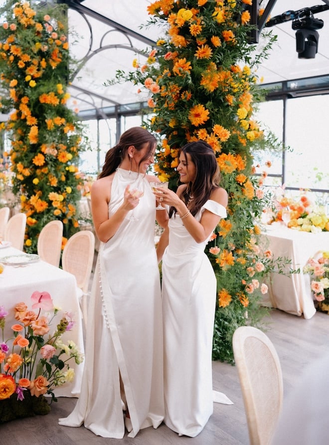 The brides smiling at each other and clinking their glasses.