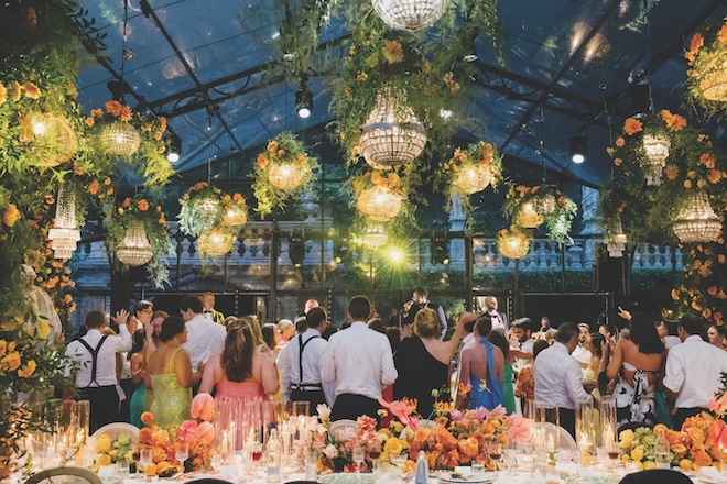 Guests dancing in the glass atrium with the chandeliers lit up.