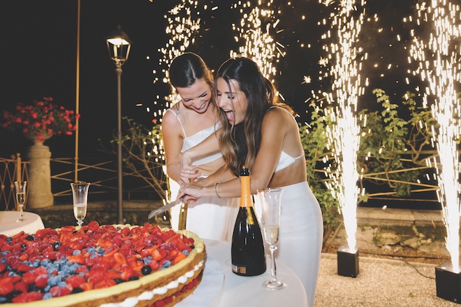 The brides cutting their fruit-covered cake with sparklers behind them.