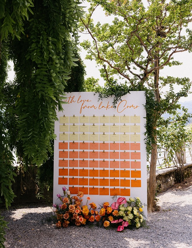 A yellow and orange wedding seating chart is displayed at the wedding reception in Lake Como, Italy.