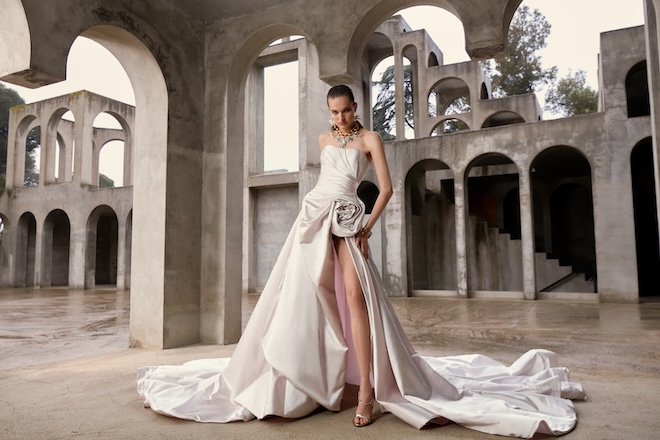 A blush structured pleated corset that cinches the waist, flowing into a voluminous ball gown skirt with a daring side slit.