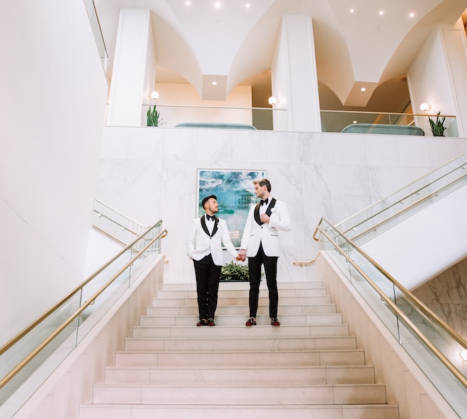 The grooms holding hands on the grand staircase at The Laura Hotel.