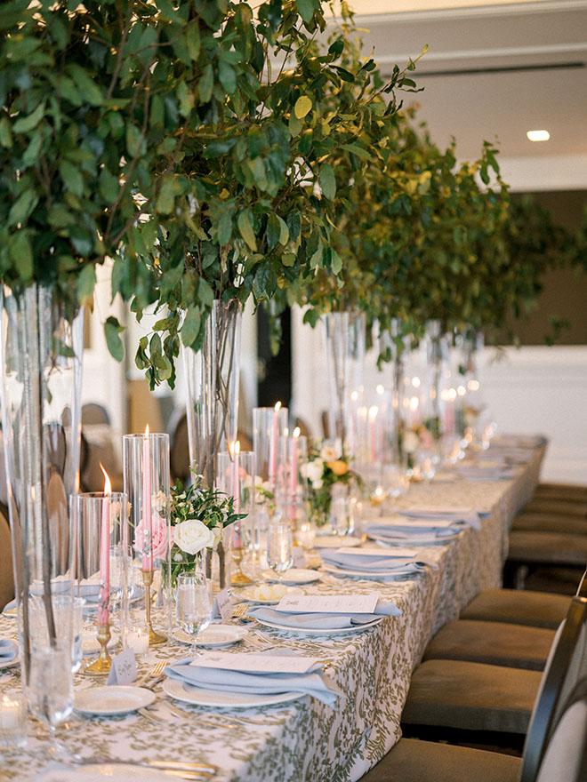 Tall greenery, pink candles and green printed linens decorate the soft pastel wedding reception in Houston. 