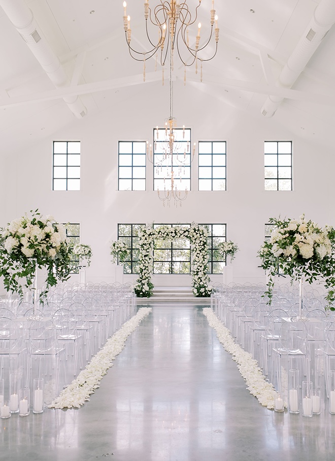 A floral arch and floral arrangements of greenery and white flowers decorate the wedding ceremony.