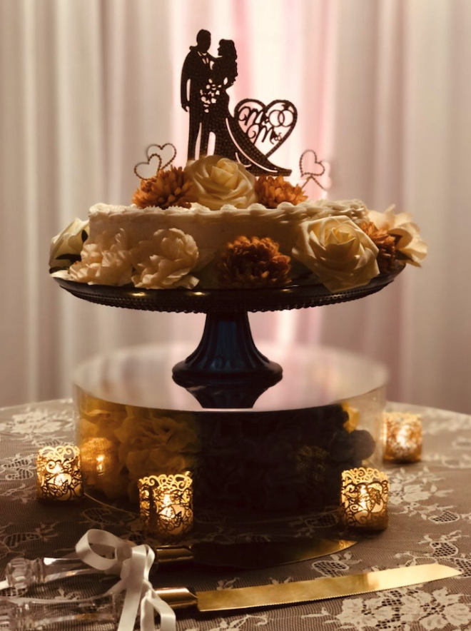 A white one-tier wedding cake decorated with florals and a bride and groom cake topper.