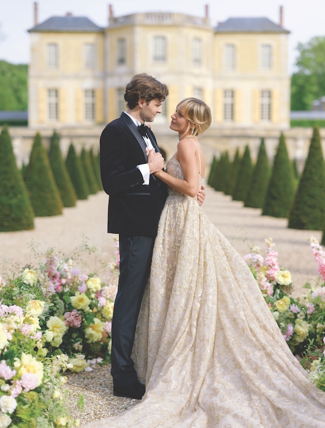 The bride and groom looking at each other with flowers surrounding their feet in front of a Chateau.