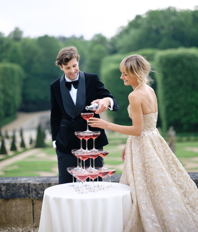 The bride and groom pouring a red drink into a tower of coupe glasses.