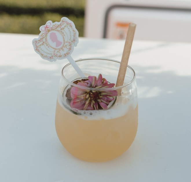 A drink with a floral garnish and a Bridgerton-inspired drink pick.