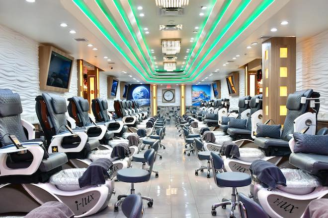 Line of salon chairs inside nail salon with green lighting above 