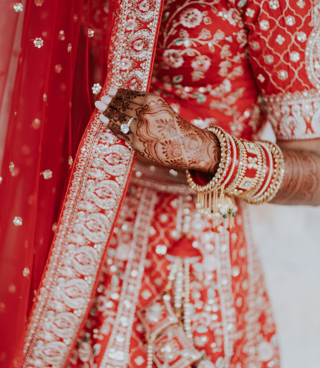 Close up of a woman's henna tattoo and she's wearing a red and gold dress while wearing red and gold bracelets on her wrist for her wedding day. 