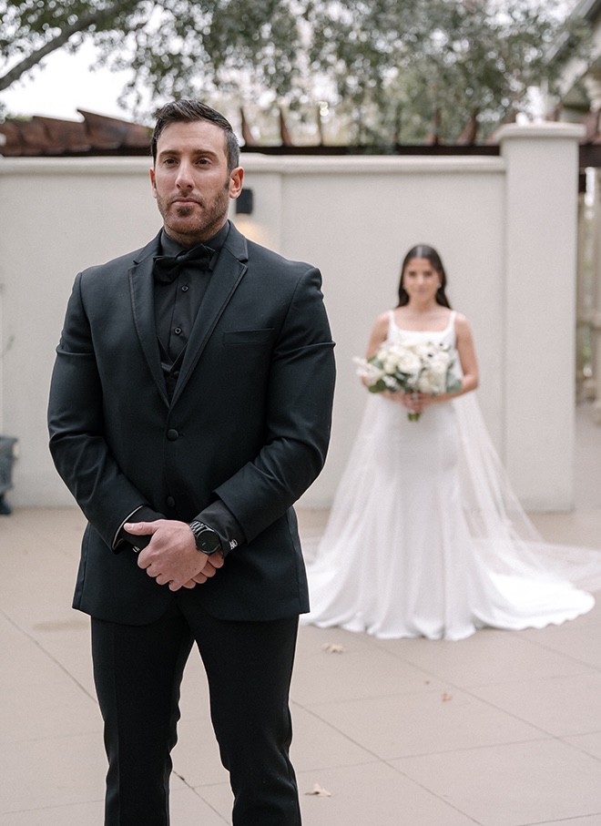 The bride stands behind the groom before their private first look. 