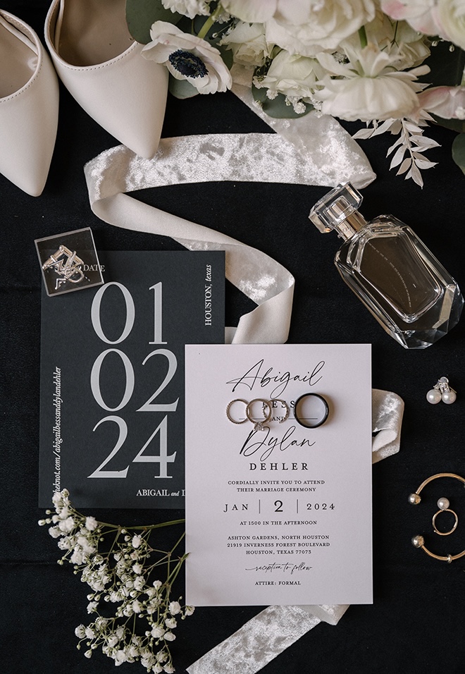The couple's wedding invitations and stationery are placed in the middle of a perfume bottle, bridal jewelry and baby's breath. 
