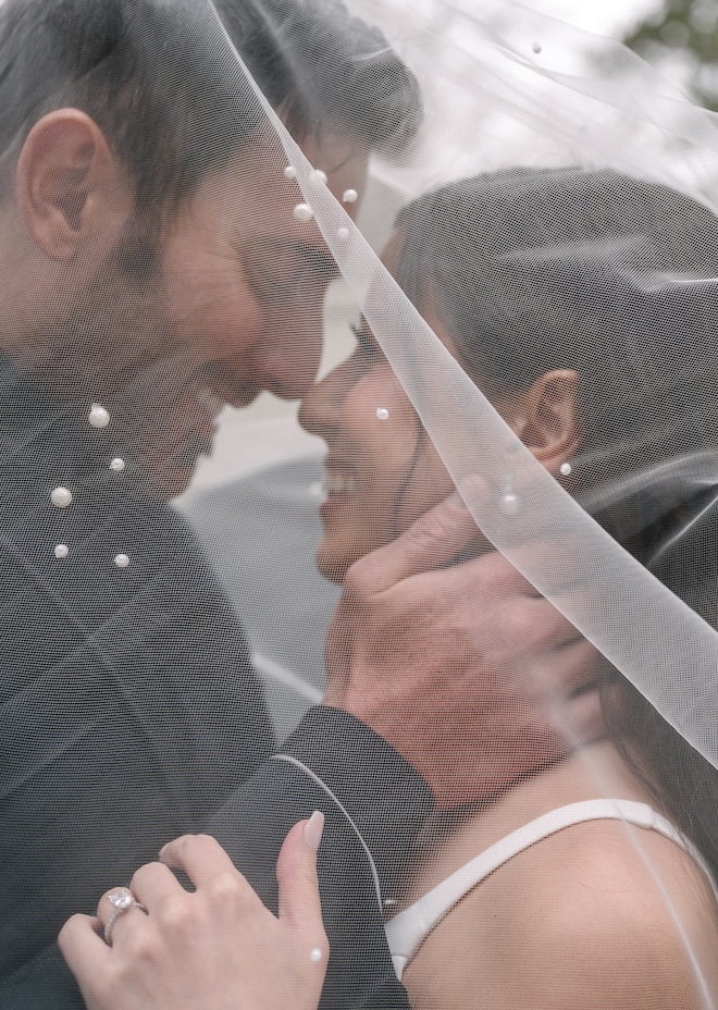 The bride and groom hold each others faces under the bride's wedding veil. 